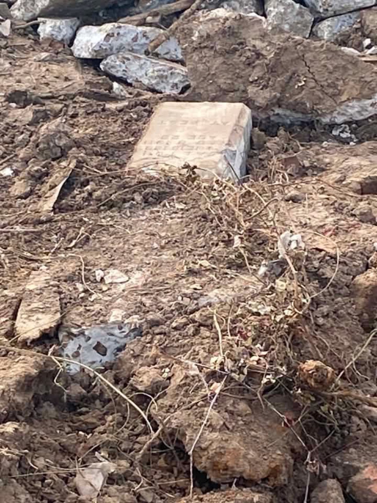 A small headstone still half-buried in dirt and rubble