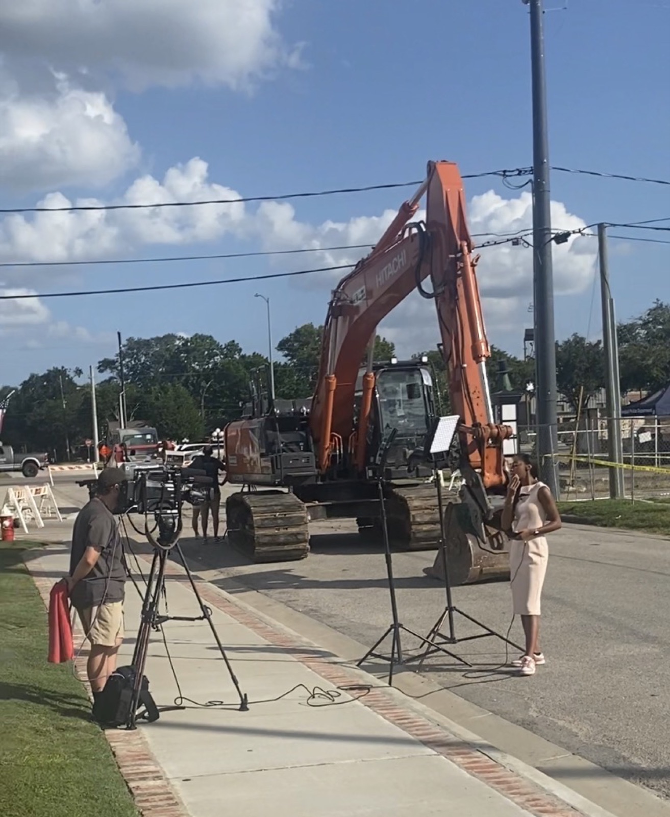 A television news crew filming a reporter at the fenced site