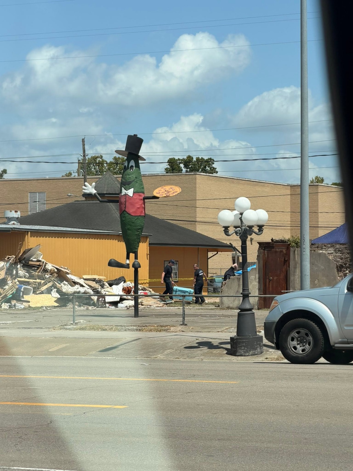 A downtown Tomball landmark statue stands over the demolition debris pile as officers work