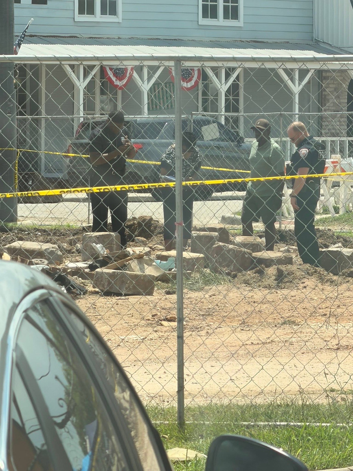 People examining slabs of stone in the churned dirt behind a chain-link fence