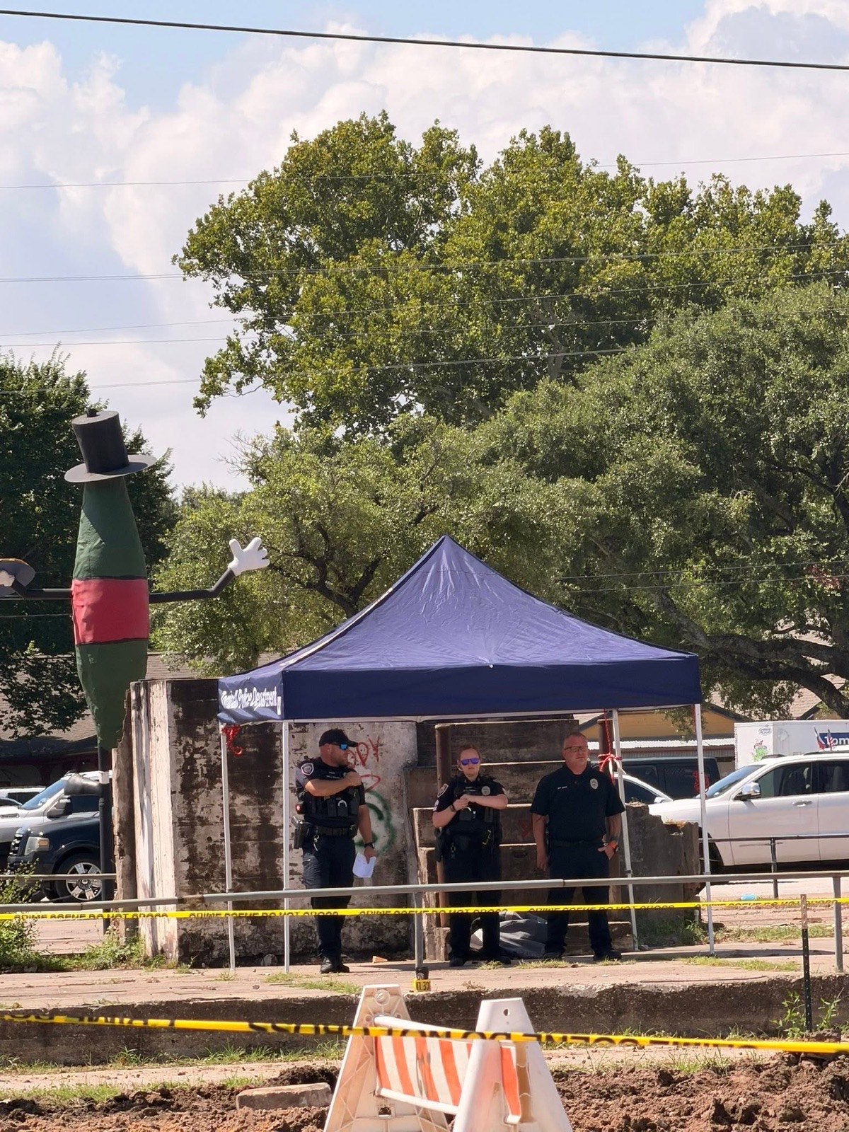 Tomball Police officers under a department tent beside the fenced site, with a landmark statue nearby